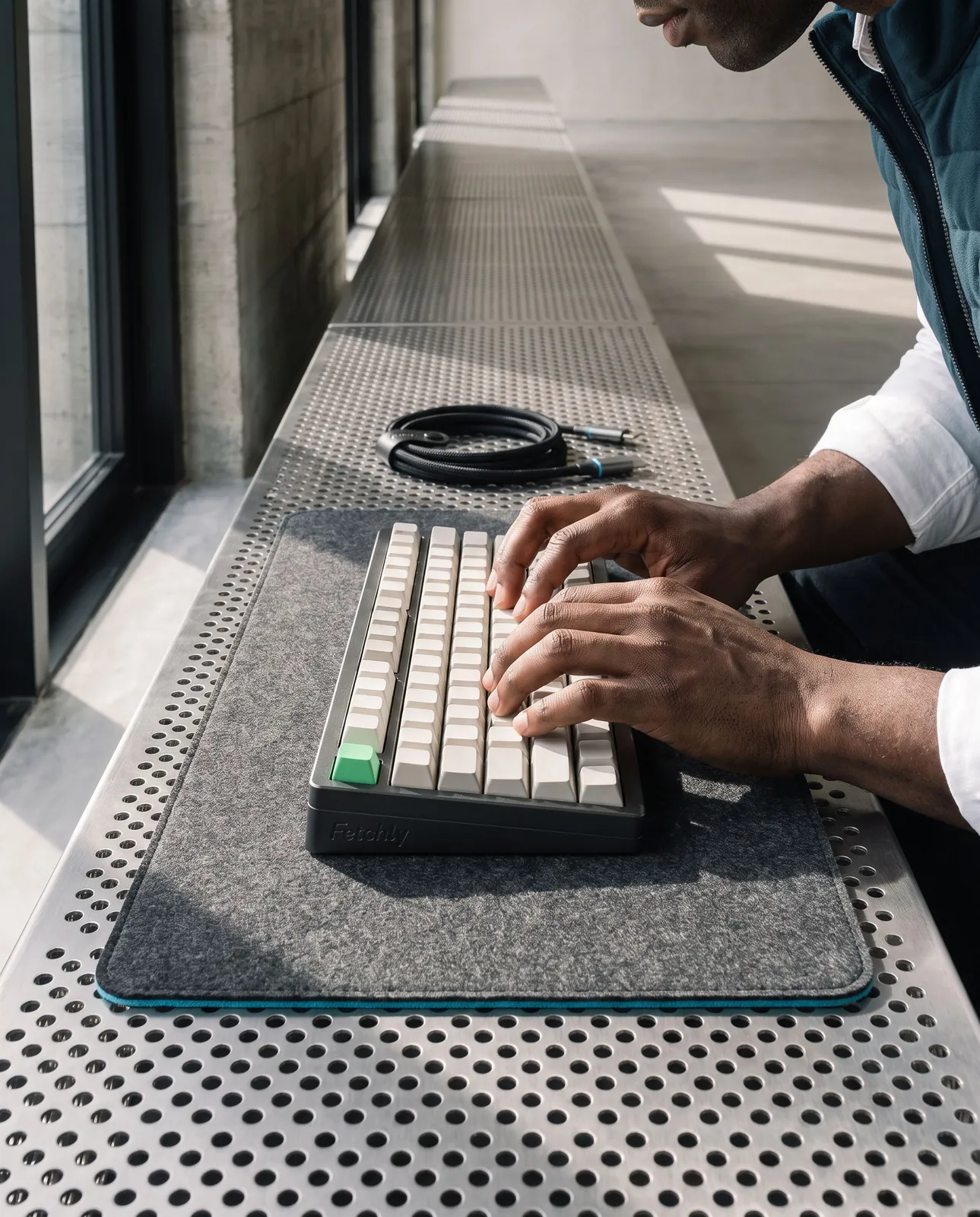 Hands typing on the keyboard over the felt mouse pad, cable coiled behind