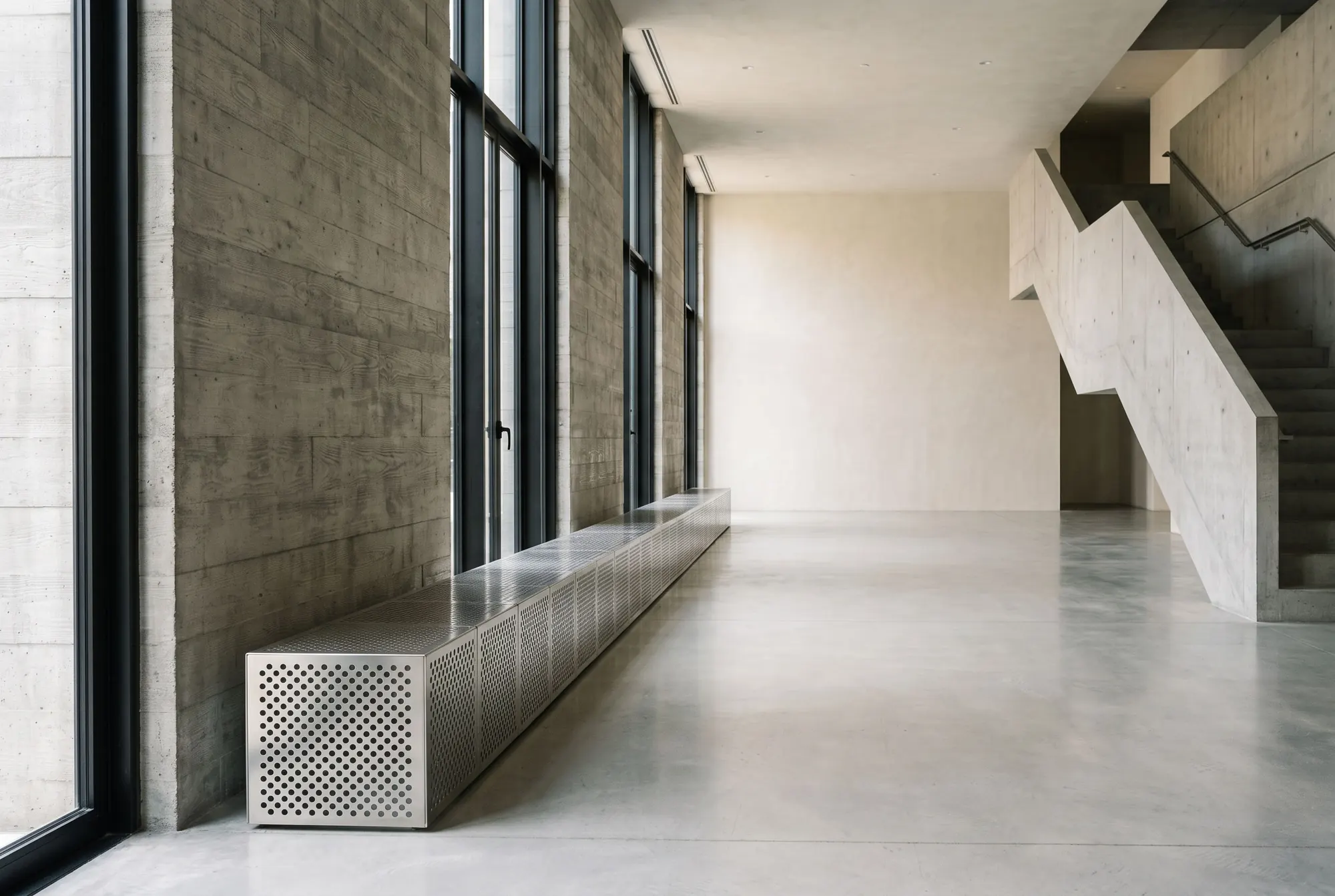 The empty concrete hall, a steel bench under tall windows