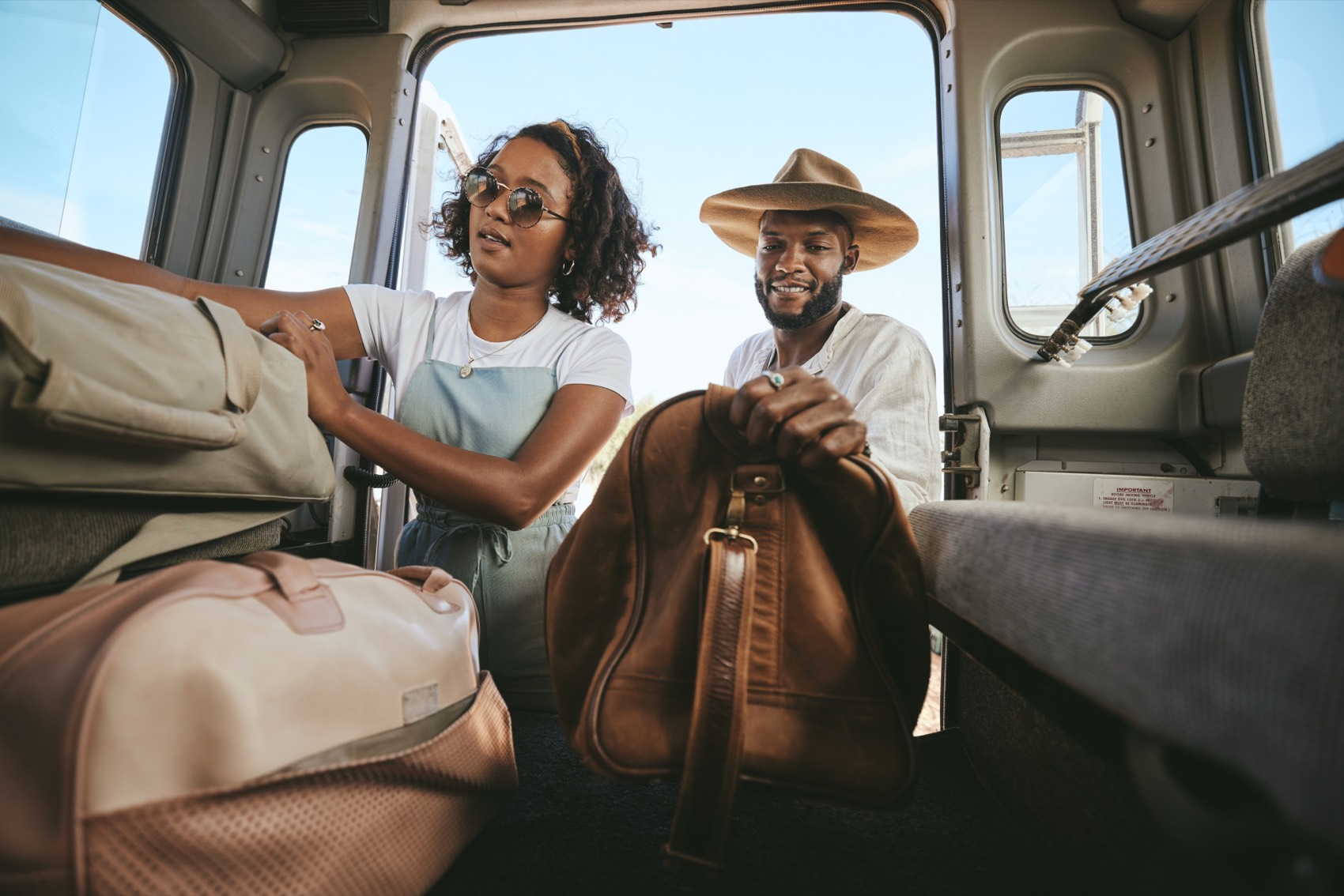 Two travelers loading leather bags into a van