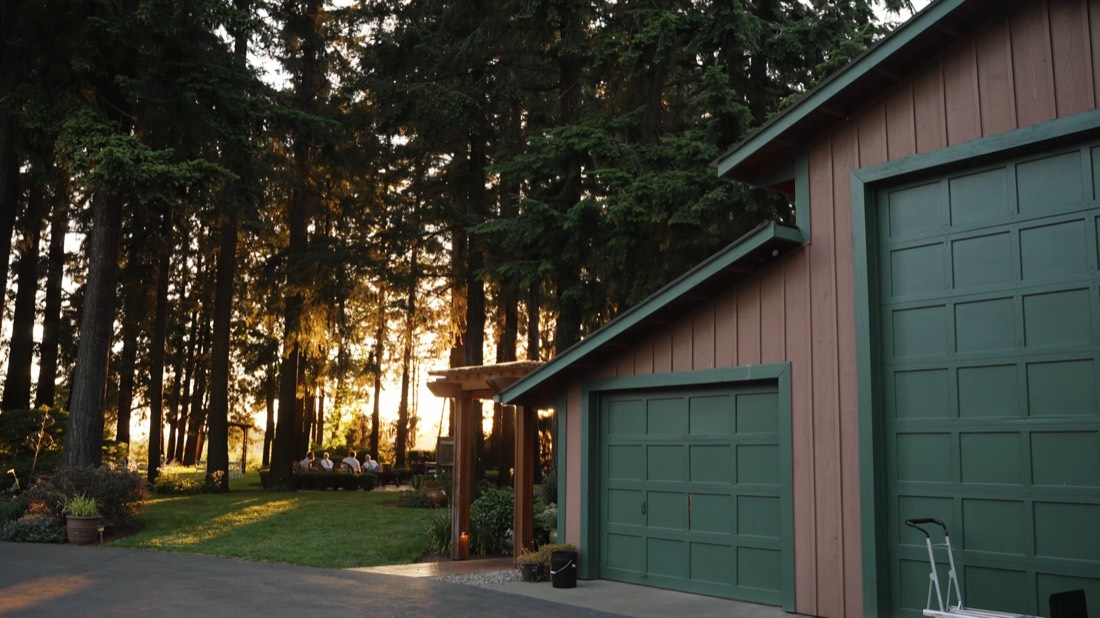A cedar garage at the edge of a forest at sunset
